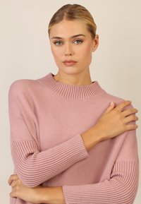 Hellrosa Strickpullover mit einem hohen gerippten Ausschnitt und gerippten Bündchen, mit einer glatten Körperstruktur und lässiger Passform.