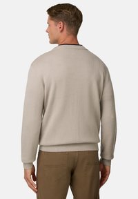 Pull beige texturé avec un col rond et des poignets côtelés, porté avec un pantalon marron. Le dos présente un design simplifié.