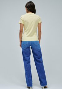 Camiseta de algodón amarilla de manga corta, combinada con unos vaqueros de mezclilla azul de lavado medio que tienen perneras rectas y bolsillos traseros.