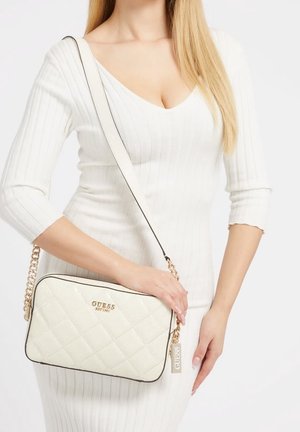 Bolso acolchado blanco con herrajes dorados, borde negro y una correa de cadena. Presenta el logo de la marca en la parte frontal y tiene forma rectangular.