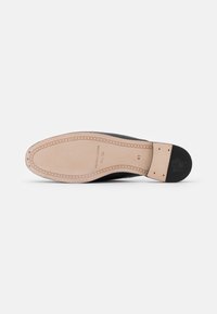 Semelle de chaussure en cuir noir avec une incrustation beige, présentant des détails cousus et un logo embossé au niveau du talon. Taille indiquée comme 41.