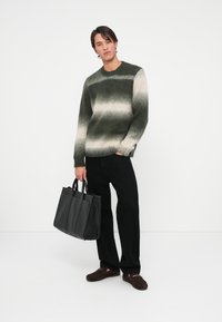 Maglione a maglia verde e beige con tonalità sfumate, maniche lunghe, pantaloni neri e una borsa a tracolla in pelle nera, caratterizzato da una consistenza morbida e una vestibilità casual.