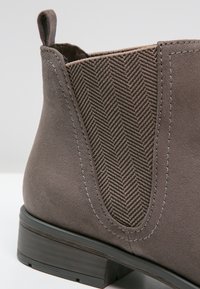 Graue Wildlederknöchelstiefel mit Herringbone-elastischen Seitenpaneelen, kontrastierenden Nähten und einer robusten schwarzen Gummisohle.