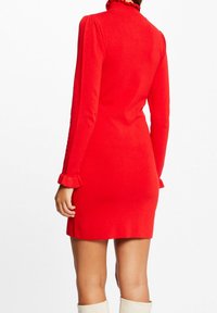 Rode aansluitende jurk met een hoge kraag en ruches bij de halslijn en manchetten. Lange mouwen, gladde textuur en een lengte boven de knie.
