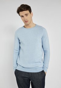 Hellblaue, strukturierte Strickjacke mit langen Ärmeln und Rundhalsausschnitt, kombiniert mit dunkelgrauen Hosen. Einfaches Design, ohne zusätzliche Muster.