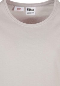 Svijetlosivi pamučni T-shirt s okruglim izrezom. Ima oznaku s uputama unutra koja prikazuje informacije o sigurnosti od vatre i veličini.
