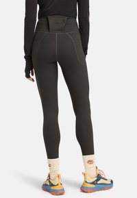 Mörkgrå höga leggings med en texturerad midja, förstärkta sömmar och två sidofickor. I kombination med färgglada utomhusskor.