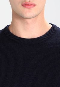 Granatowy sweter dzianinowy z prążkowanym okrągłym dekoltem. Materiał wydaje się miękki o gładkiej strukturze, idealny do codziennego noszenia.