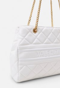 Sac à main blanc matelassé avec logo "VALENTINI" en relief, doté de chaînes dorées et d'un design structuré. Surface lisse et texturée.