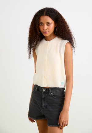 Short-sleeve, cream knit top with a round neckline and front buttons. Paired with high-waisted black denim shorts featuring frayed edges.