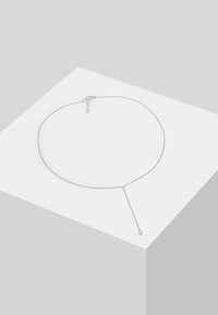 Collier chaîne en argent au design minimaliste. Présente une forme élancée, une texture lisse et un pendentif en goutte avec un détail en boucle.