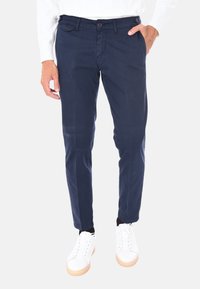 Chino navy in cotone misto, caratterizzati da una vestibilità slim con due tasche laterali e chiusura a bottone, abbinati a sneakers bianche.
