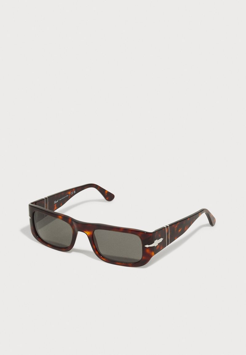 Gafas de sol carey con lentes oscuros, forma rectangular, montura gruesa y detalles plateados en las patillas. Textura suave y acabado brillante.