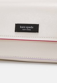 Portafoglio in pelle testurizzata beige chiaro con etichetta nera che recita "kate spade NEW YORK." Presenta lievi cuciture decorative rosa lungo il bordo.