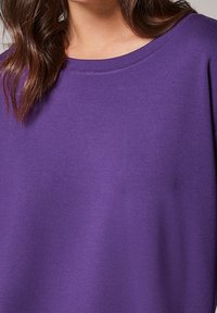 Fialový krátký rukáv top vyrobený z jemné tkaniny s širokým kulatým výstřihem. Design se vyznačuje hladkou, plochou texturou s minimálním šitím.