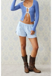 Top corto a costine azzurro chiaro con bordi bianchi, abbinato a pantaloncini a quadretti azzurro chiaro e stivali marroni in pelle fino al ginocchio.