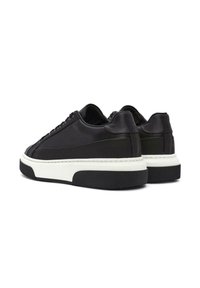 Sneakers in pelle nera con una texture liscia, caratterizzati da una soletta bianca e una robusta suola in gomma nera. Presentano lacci piatti e accenti minimalisti.