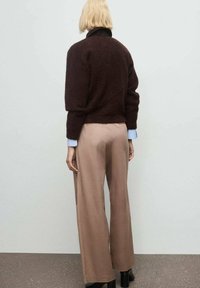 Bruine fuzzy trui met een hoge kraag, gecombineerd met beige wijde broekspijpen. De outfit heeft een lichtblauw manchetdetail.