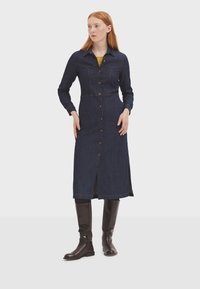 Vestido camisero de mezclilla en azul oscuro, con cierre de botones en la parte delantera, mangas largas, cuello, aberturas laterales y detalles de costura en contraste.