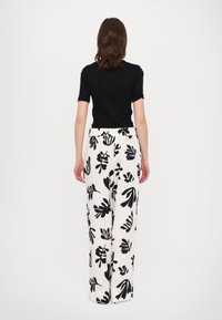 Black short-sleeve top paired with white wide-leg pants featuring a black floral pattern. The pants have an elastic waistband.
