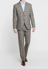 Grijs ruitpak bestaande uit een colbert met twee knopen en bijpassende broek, gecombineerd met een lichtblauw overhemd. Bruine schoenen maken de look compleet.