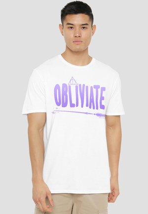 Young man wearing a white t-shirt with purple text "OBLIVIATE" and a wand graphic underneath on a plain light background.