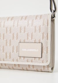 Béžová peněženka s raženým vzorem a štítkem loga, obdélníkový tvar, textilní syntetický materiál, zapínání na zip a kontrastním lemem.