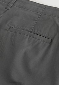 Détail de la poche arrière d'un pantalon en tissu gris foncé avec une poche passepoilée simple et des coutures apparentes.