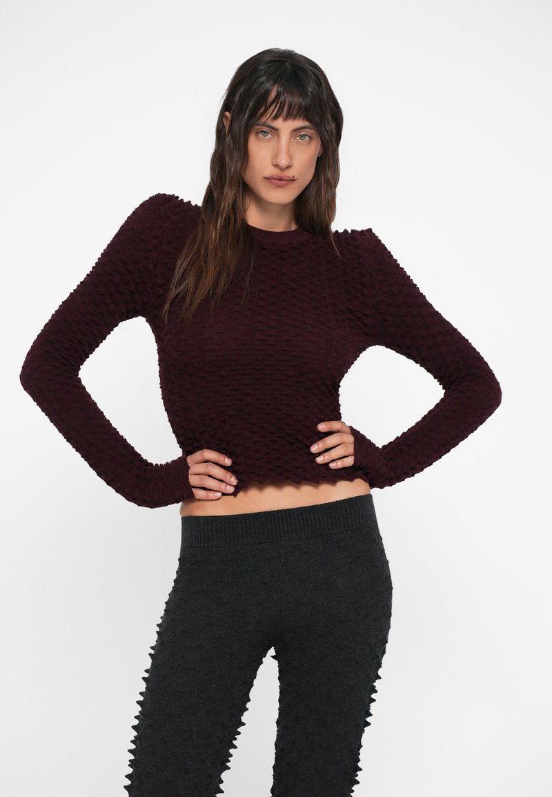 Bordeaux gebreide trui met een getextureerd, 3D-patroon en lange mouwen, in combinatie met donkergrijze leggings met geribbelde tailleband en een verhoogd ontwerp.