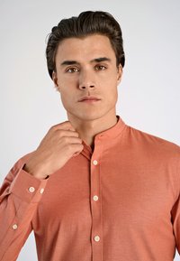 Camisa de hombre de manga larga en color coral, fabricada en un material ligero. Presenta un cuello alto, una tapeta de botones y puños abotonados con una textura suave.