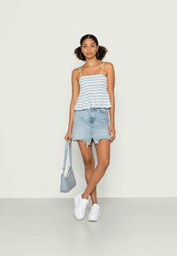 Camisola risca azul clara com alças finas, emparelhada com uma saia de ganga desgastada. Modelo usa ténis brancos e leva uma bolsa cinza clara.