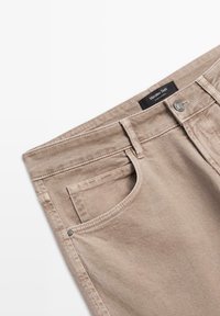 Beżowe dżinsy z bawełny o średnim stanie, z kieszenią z przodu, detalami w stębnowaniu oraz markową czarną metką przy pasie.