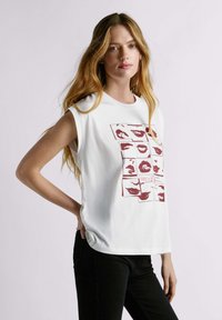 Witte mouwloze T-shirt met meerdere rode lippen grafische ontwerpen, ronde halslijn en zachte stof, gecombineerd met zwarte broek.