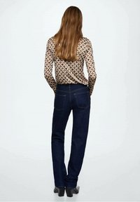 Langärmliges, gemustertes Oberteil mit geometrischem Design in Beige und Braun, kombiniert mit dunkelblauen Jeans, von hinten betrachtet.