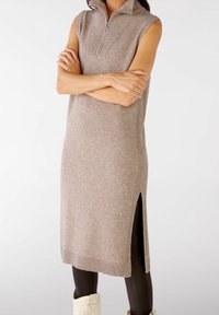 Robe sans manches en tricot de couleur beige clair avec un col haut et une fermeture éclair. Présente des fentes sur les côtés et des accents côtelés pour plus de texture.