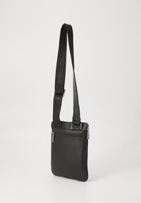 Sac en cuir noir à bandoulière avec une finition texturée, comportant une poche zippée à l'avant et une bandoulière ajustable portant l'inscription "Valentino."