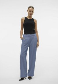 Zwarte geribbelde tanktop gecombineerd met lichtblauwe wijde broek. De broek heeft zijzakken en een getailleerde pasvorm. Zwarte puntige hakken maken de look af.