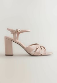 Sandale à talons hauts en cuir verni nude avec bride à la cheville, boucle dorée et brides croisées à l'avant sur un talon bloc.