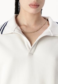 Maiou alb cu o suprafață texturată, cu guler în dungi bleumarin și o deschidere parțială. Include un colier din lanț împletit auriu.