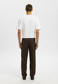 Witte T-shirt met korte mouwen en een klassieke snit, gecombineerd met bruine recht-toe-rechtaan broek met een achterzak en een gladde textuur.