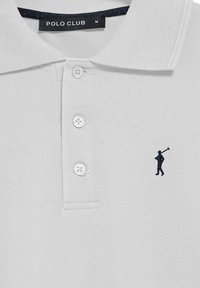 Ljusgrå pikétröja i texturerad tyg, med en tvåknapps knäppning och en liten mörkblå broderad figur på bröstet. "POLO CLUB"-etikett synlig.