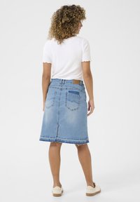 Fustă A-line din denim cu tiv brut, spălare albastră deschisă și două buzunare la spate. Asortată cu un top alb cu mânecă scurtă și pantofi bej.