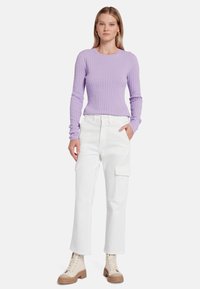 Top lungo a maniche lunghe in maglia a coste lilla abbinato a pantaloni cargo bianchi. Il modello indossa stivaletti color crema con suola spessa.