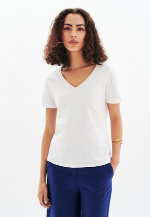 T-shirt blanc à col en V en coton doux avec des manches courtes, associé à un pantalon bleu ; présente un design simple et épuré.