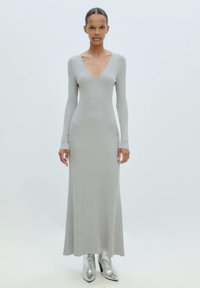 Langaarmige V-hals jurk in lichtgrijze ribbeltricot, aangesloten bij de taille, uitlopend aan de zoom. Gecombineerd met metallic zilveren enkellaarsjes.