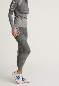 Top atlético gris con diseño texturizado, leggings gris a juego con acentos a rayas, combinados con zapatillas deportivas blancas y azules.