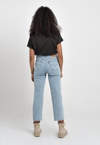 Svart kortärmad t-shirt i kombination med ljusblå högmidjade jeans, med en klassisk femficksdesign och sömnadsdetaljer.