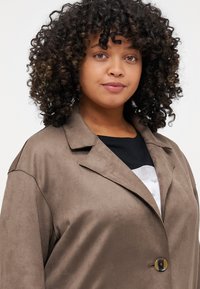 Brown faux suede jacket with a notched collar, single button closure, and visible stitching details. Texture appears smooth and soft.