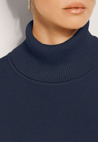 Navy-blaues, geripptes Rollkragenoberteil mit hohem Kragen und glatter Textur, das die Elastizität des Stoffes und das klare Design betont.