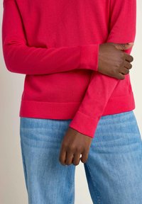 Fitted long-sleeve sweater in bright pink fabric, paired with light blue denim jeans. The sweater features ribbed cuffs and hem.